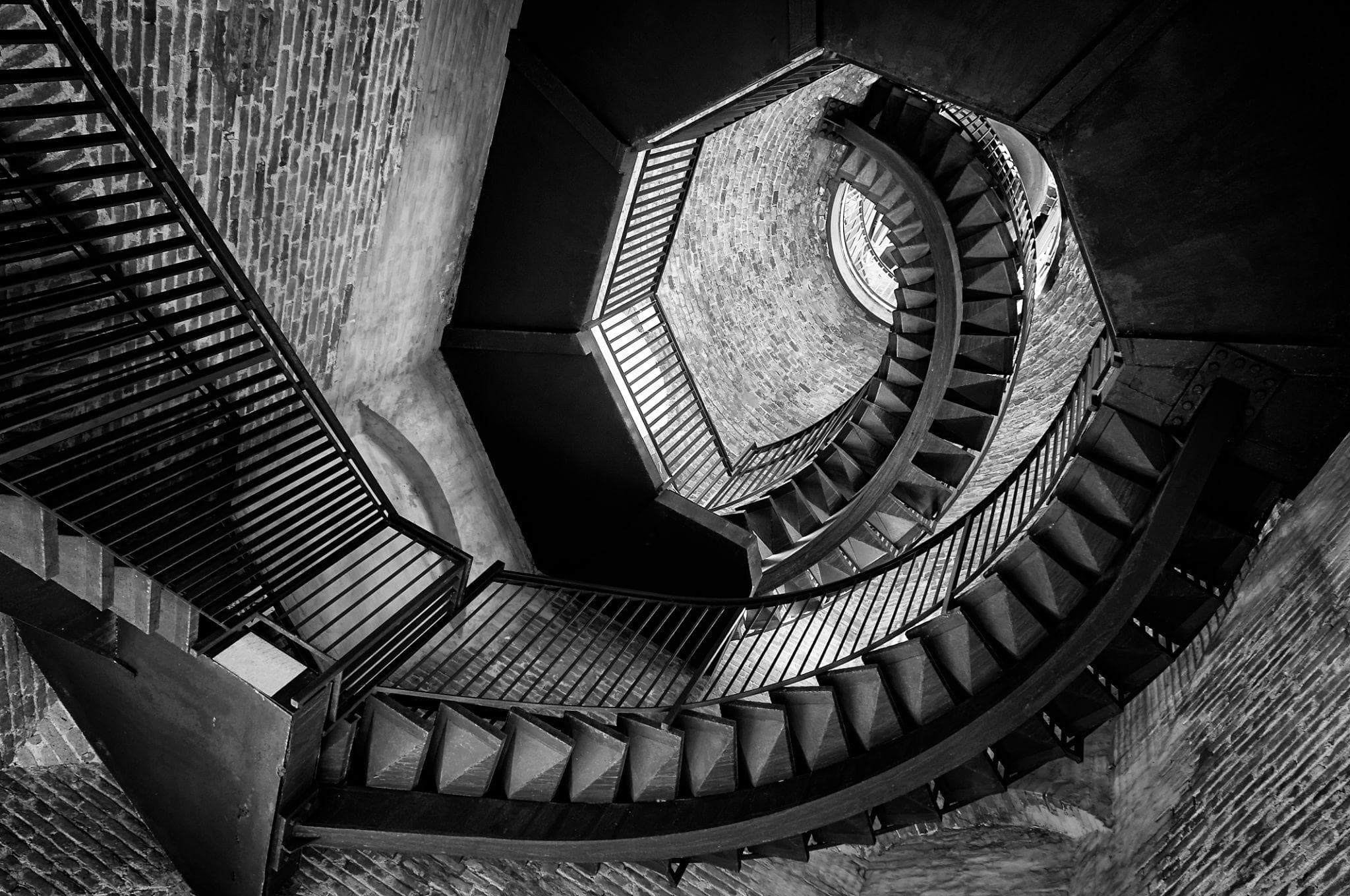 A spiral staircase viewed from above, descending into depth